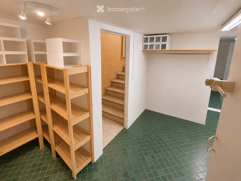 Empty room with green tiled floor, white walls, wooden shelving units, and a small staircase leading to another area.