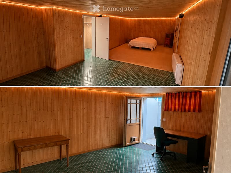 Two connected rooms with wooden walls and green tiled flooring. The first room contains a bed, nightstand, and a small table. The second room features a desk, chair, and a curtained window.