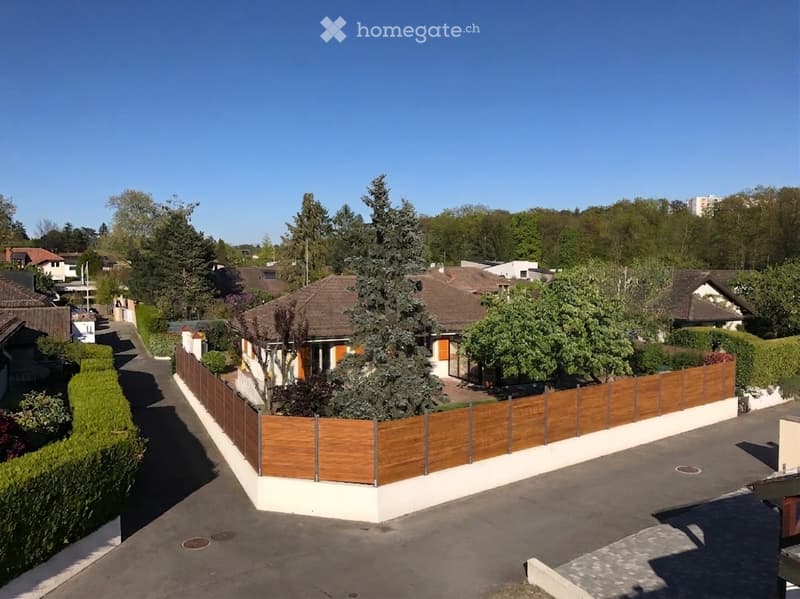 A two-story house with a brown tiled roof, surrounded by a wooden fence and trees, located in a residential neighborhood.