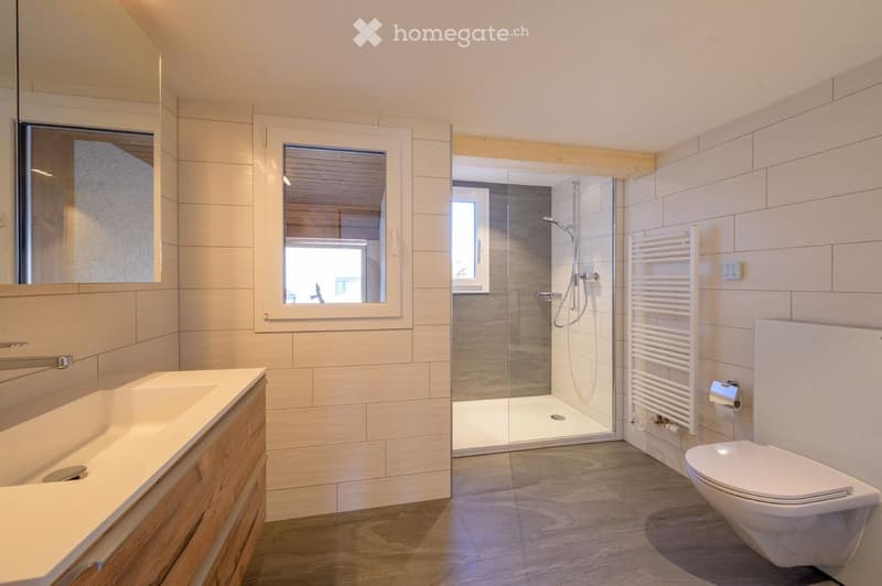 Modern bathroom with a white sink, toilet, glass-enclosed shower, and a white radiator. The walls are tiled in light beige, and the floor is wooden.