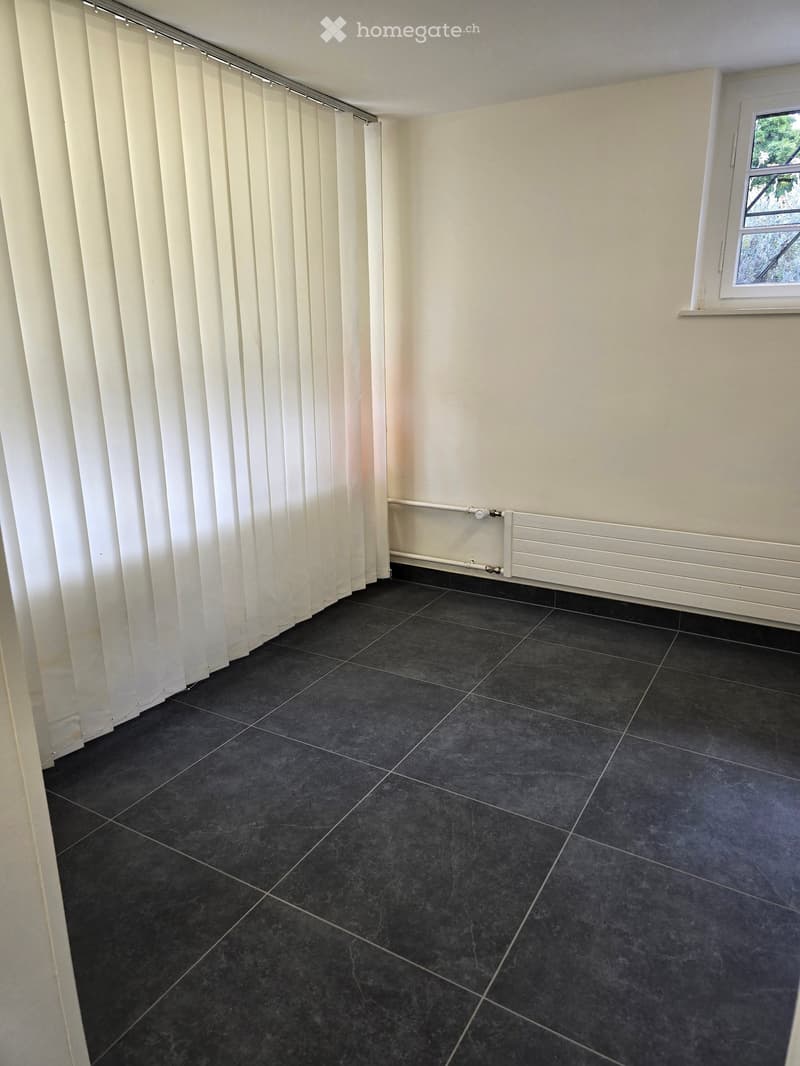 Empty room with dark tiled floor, white walls, a window with blinds, and a radiator.