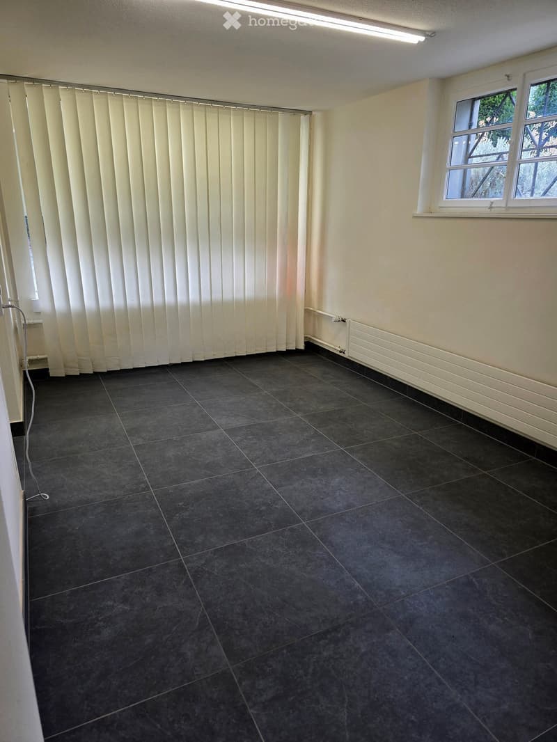 Empty room with dark tiled floor, white walls, and a window with blinds. No furniture or equipment present.