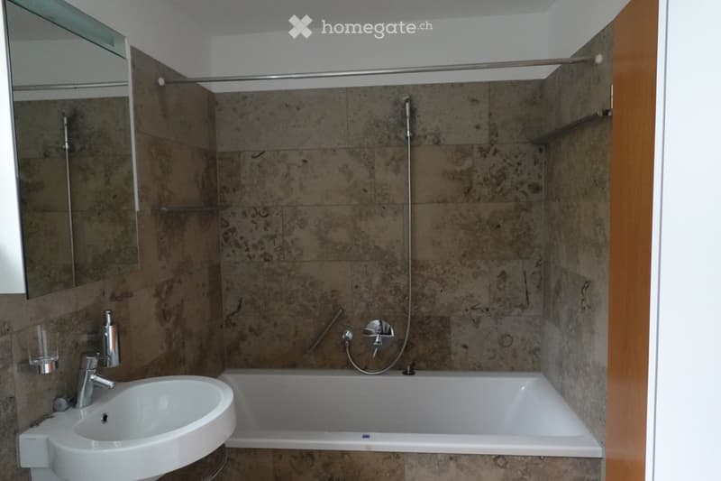 Bathroom with marble tiles, white sink, bathtub, and shower area.