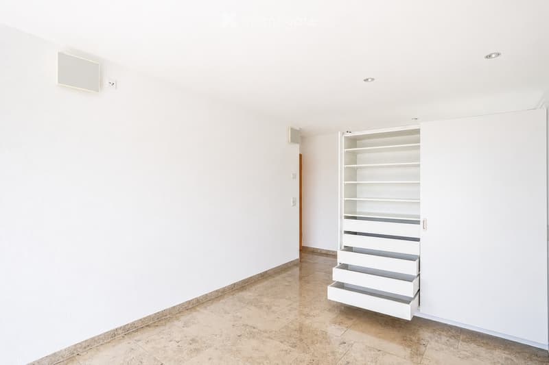 Empty room with white walls, tiled floor, and a built-in white storage unit with shelves and drawers.