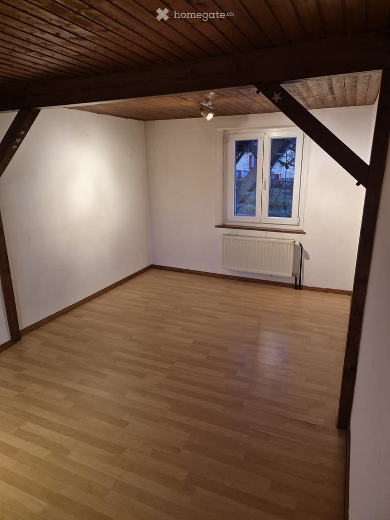 Empty room with wooden flooring, white walls, and a window with a radiator below it.