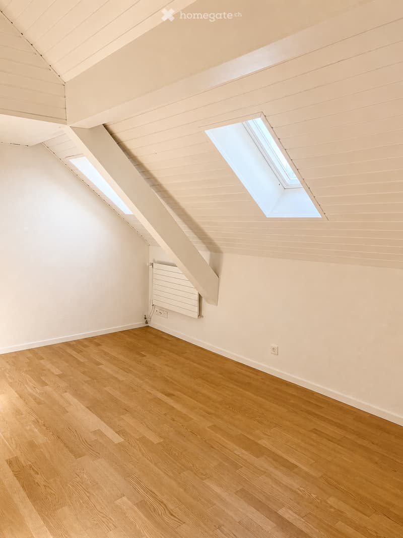 Empty attic room with wooden flooring, white walls, and skylight windows. No furniture or equipment present.
