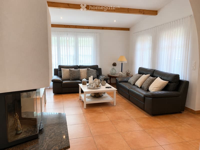 Modern living room with two black leather sofas, a white coffee table, a fireplace, and decorative items including candles and a vase.