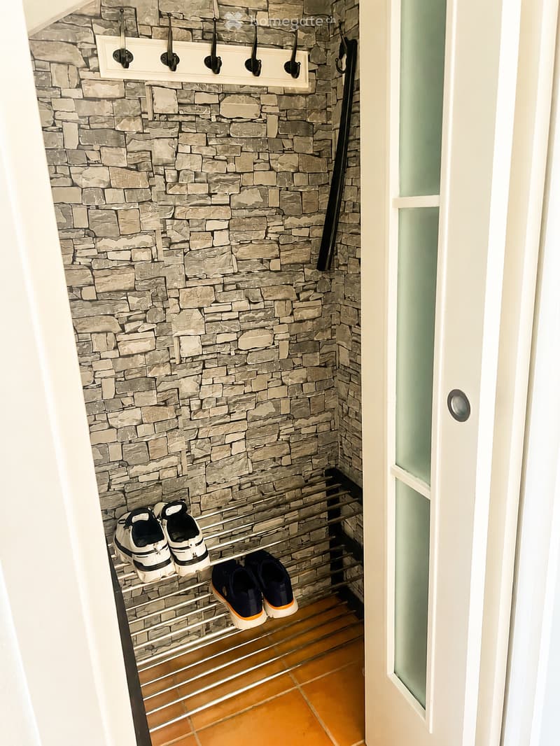 A small hallway with stone-patterned walls, a metal shoe rack holding several pairs of shoes, and a white door with a frosted glass panel.
