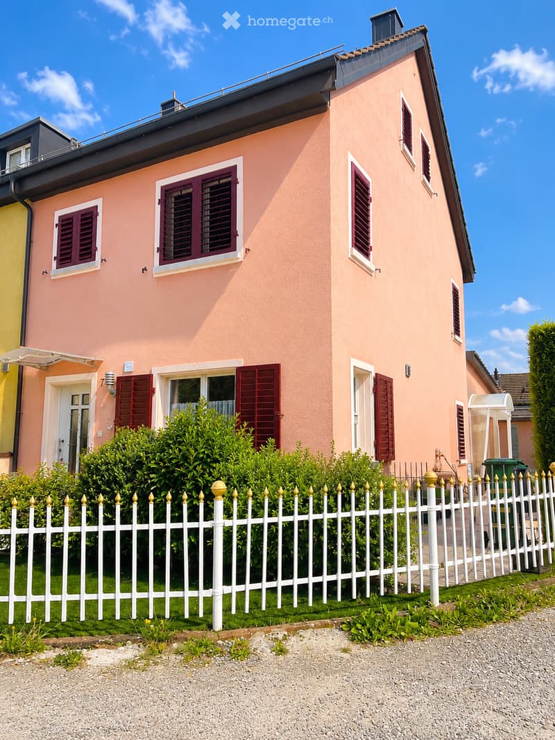 Pink two-story house with white-framed windows and red shutters, surrounded by a white picket fence and greenery.