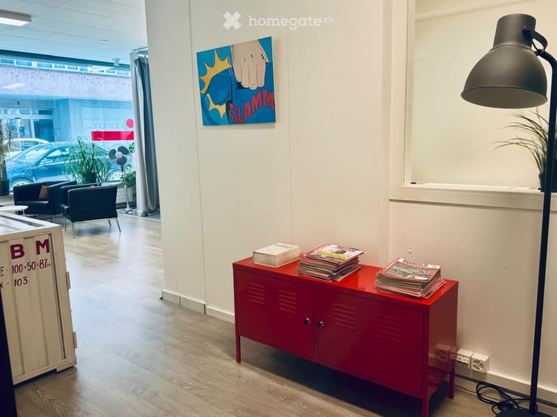 Modern interior with a red cabinet holding magazines, a floor lamp, chairs, and a fan visible in the background.