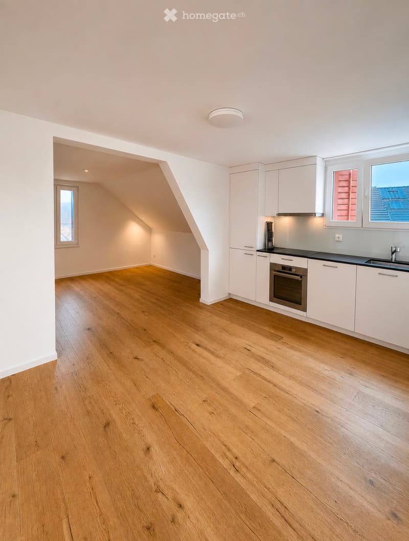 Modern kitchen with white cabinets, black countertops, and wooden flooring. Features an oven, sink, and ample natural light from windows.