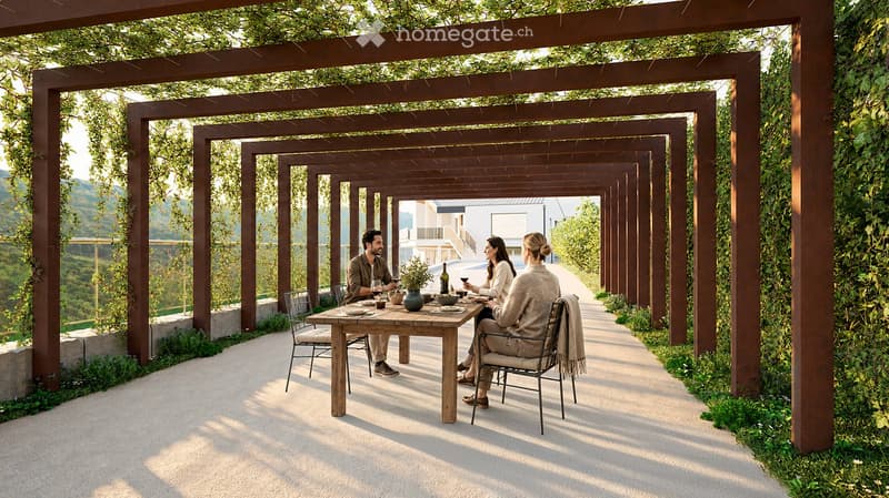 Outdoor dining area with wooden table, chairs, and a pergola covered with greenery, overlooking a scenic valley.