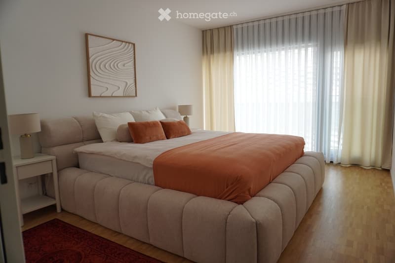 Modern bedroom with a large bed, beige sofa, nightstand with lamp, and a decorative picture frame on the wall.