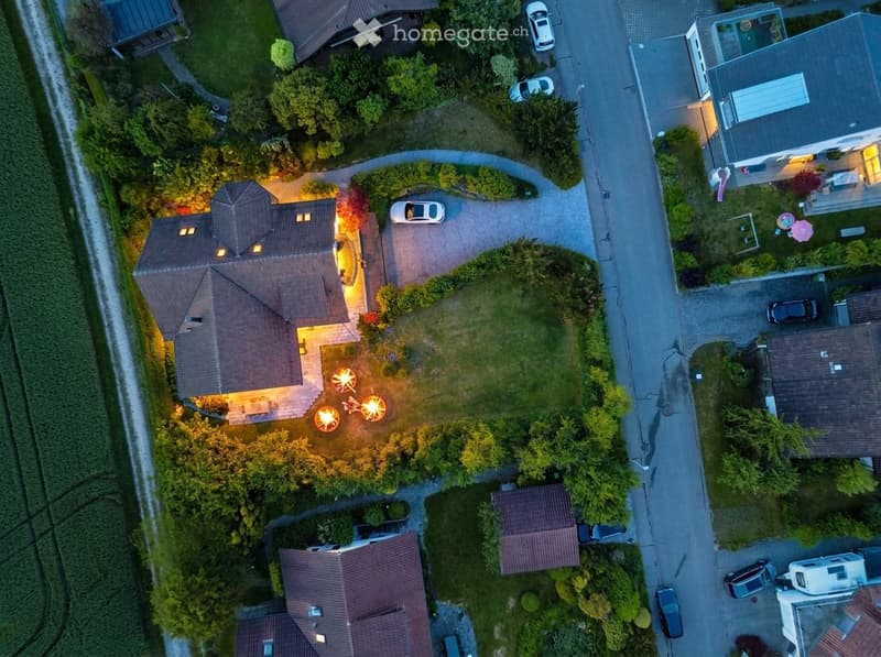 Aerial view of a residential area with multiple houses, well-lit driveways, parked cars, and landscaped gardens.