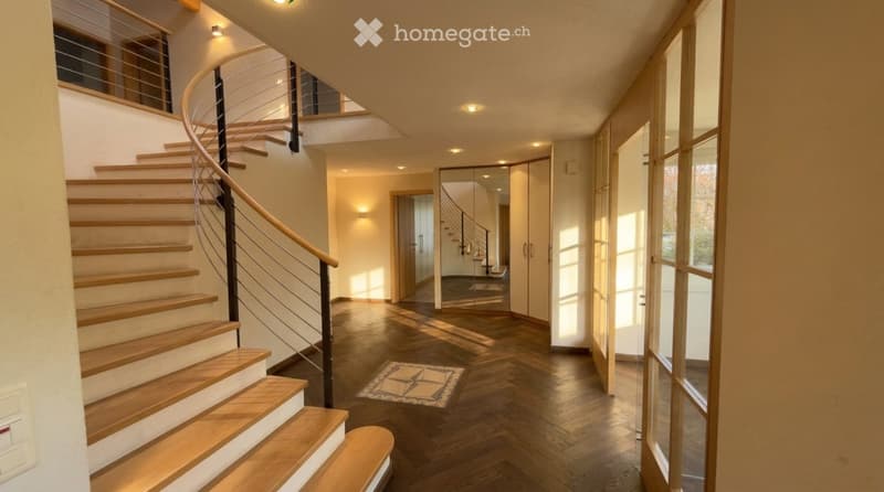 Modern hallway with wooden flooring, a curved staircase with wooden steps and a metal railing, recessed lighting, and large windows allowing natural light to enter.