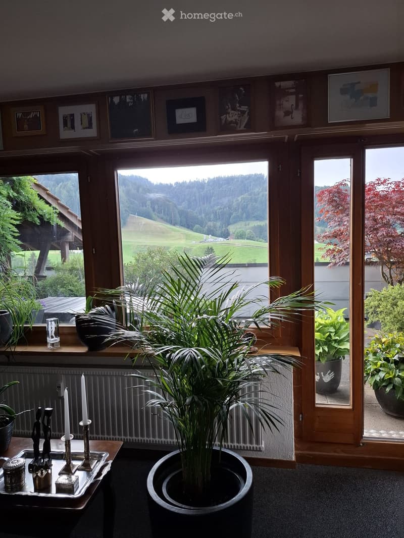 Bright living room with large windows offering a scenic view, decorated with plants, candles, and artwork.