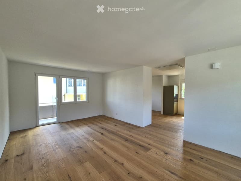 Empty room with wooden flooring, white walls, and a sliding glass door leading to a balcony.