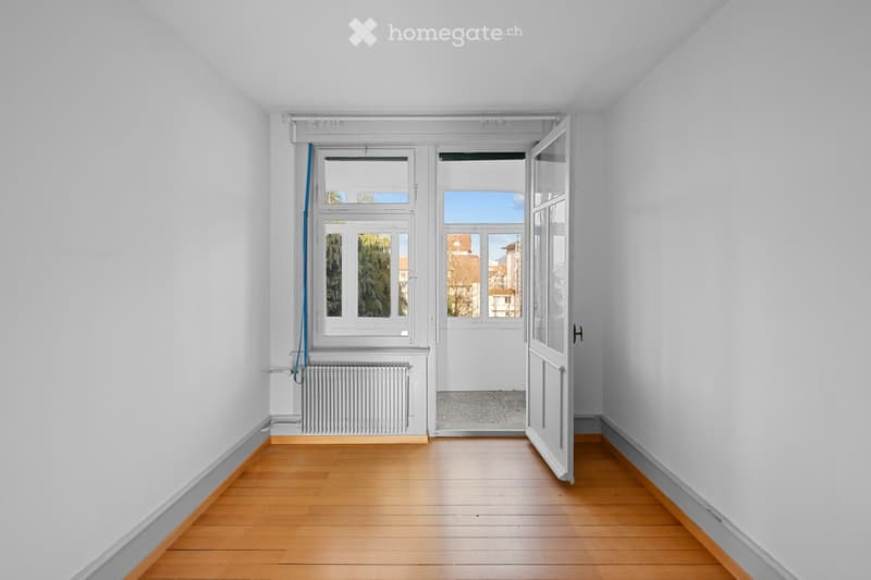 Empty room with wooden flooring, white walls, large windows, and a door leading to an outdoor area.
