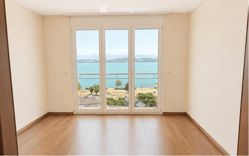 Empty room with wooden flooring and large glass doors opening to a balcony with a scenic sea view.