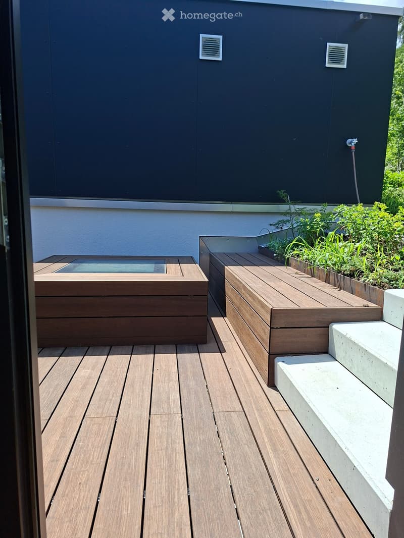 Wooden deck with built-in seating and small raised garden bed, featuring a modern design with dark walls and white accents.