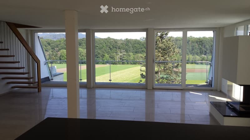 Bright, open living space with large glass doors leading to a balcony, wooden staircase, and tiled floor.