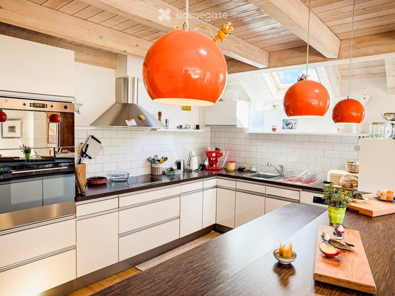 Modern kitchen with white cabinets, stainless steel appliances, and pendant lights. Features a central island with a wooden countertop, a sink, and various kitchen tools and appliances.
