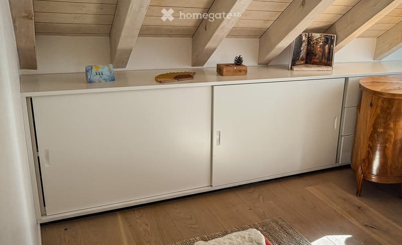 A small, modern room with white cabinets, a wooden stool, and various decorative items on the counter, including a picture frame, a book, and a small wooden box.
