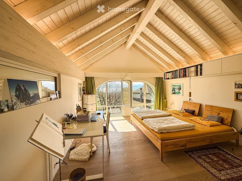 Bright, wooden-framed bedroom with slanted ceilings, large windows, a double bed, desk, and artwork.