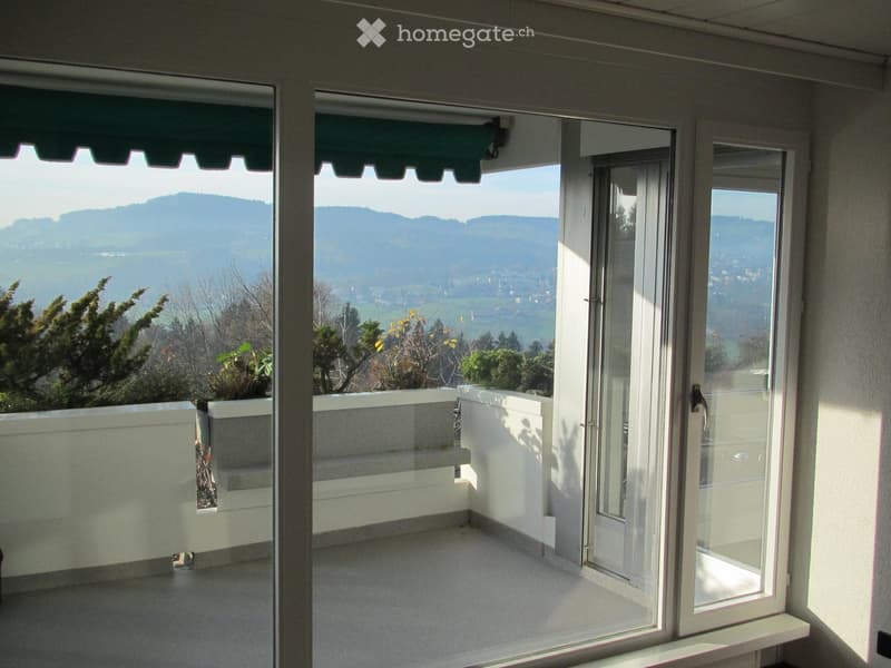 Balcony with large glass doors, white railings, and a scenic mountain view.