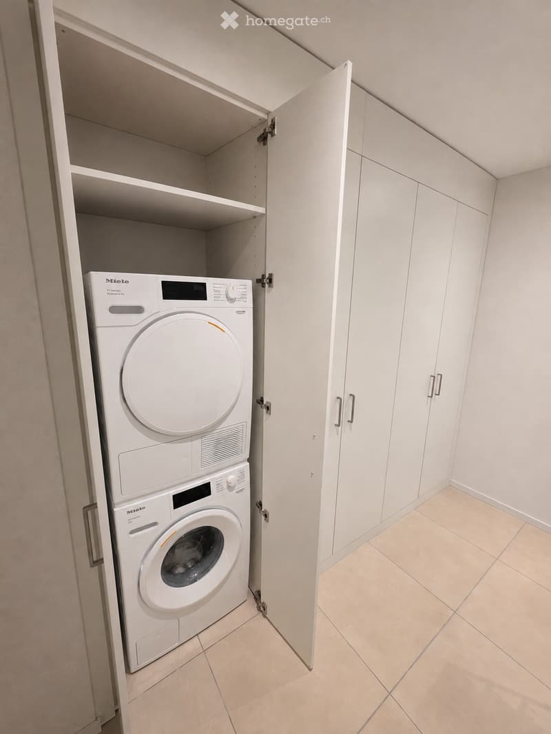A compact bathroom with a built-in laundry area featuring a white washing machine and dryer unit within a cabinet.