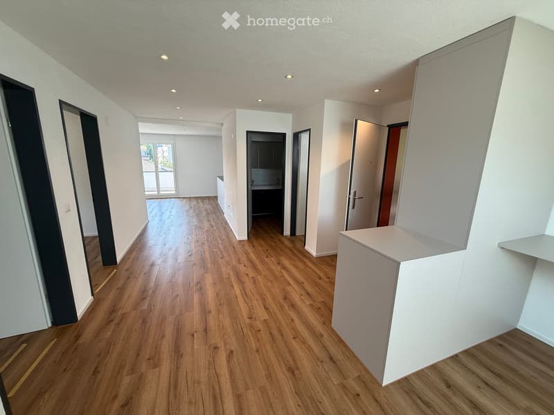 Empty hallway with wooden flooring, white walls, and several doors leading to different rooms.