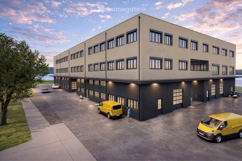 A modern two-story building with a flat roof, large windows, and a spacious parking area with several vans and a person walking.