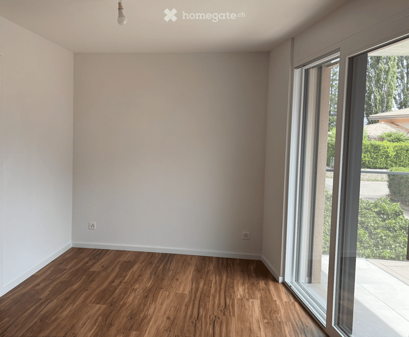 Empty room with wooden flooring, white walls, and large glass sliding doors leading to a balcony or outdoor area.