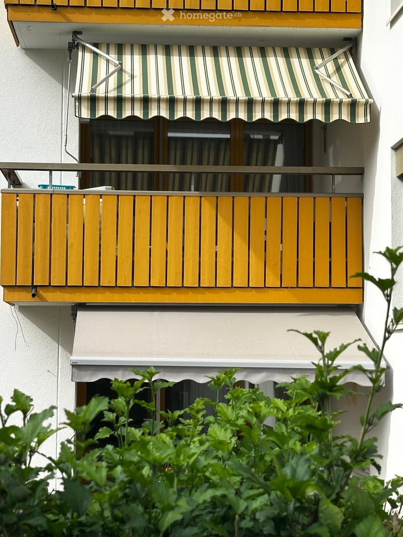 Balcony with wooden railings, striped awning, and white exterior wall.