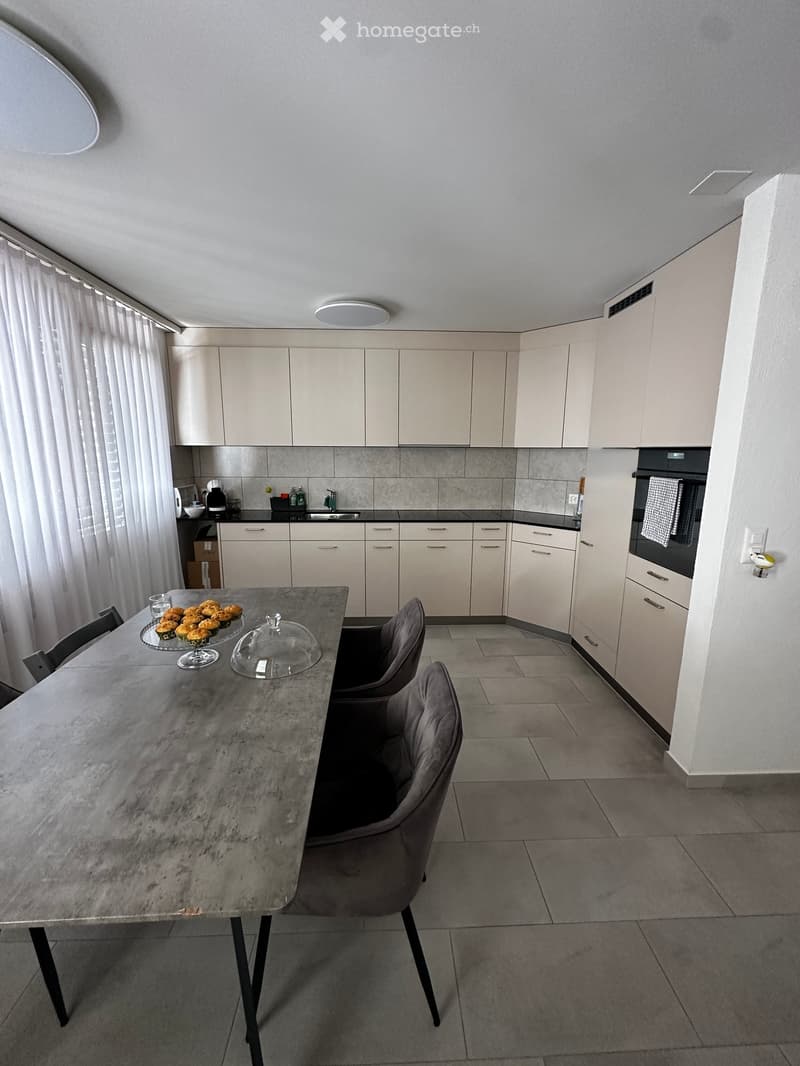 Modern kitchen with light-colored cabinets, a central island table with chairs, and various appliances including an oven and sink.