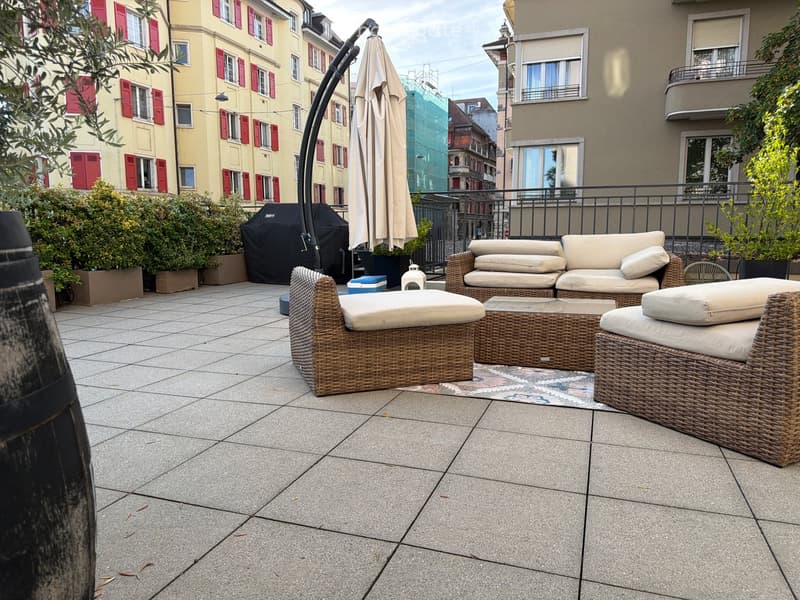 Balcony with wicker furniture, including a sofa, chairs, and a table, along with an umbrella and potted plants.