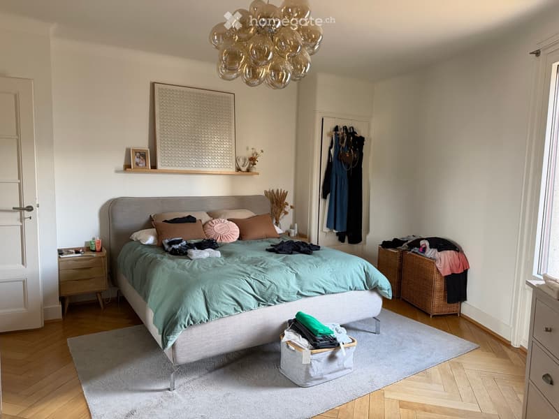 Modern bedroom with a large bed, nightstand, mirror, wicker baskets, and a decorative balloon chandelier.