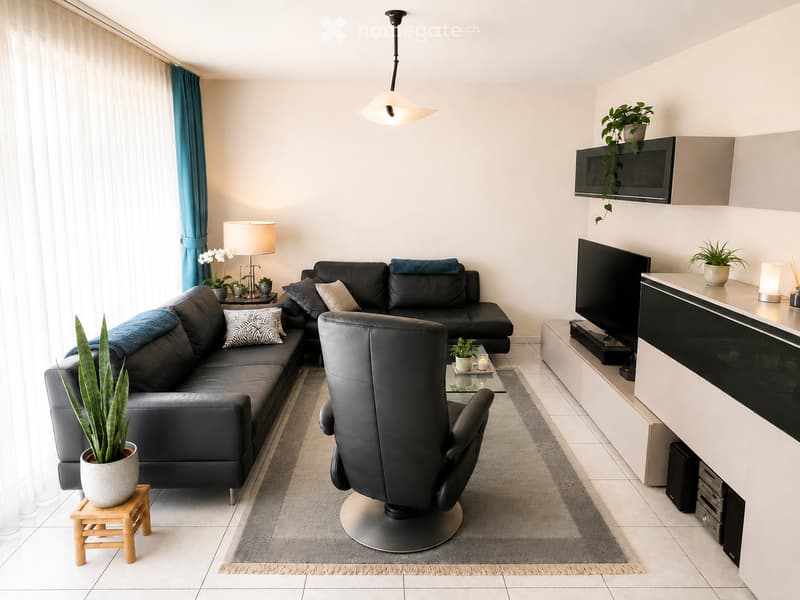 Modern living room with a black sectional sofa, a leather armchair, a glass coffee table, a wall-mounted TV, and several potted plants.