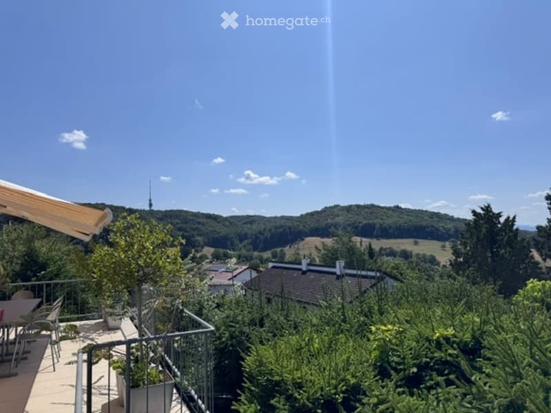 Balcony with a scenic view of a valley, trees, and houses below. Includes a small table and chairs, potted plants, and a railing.