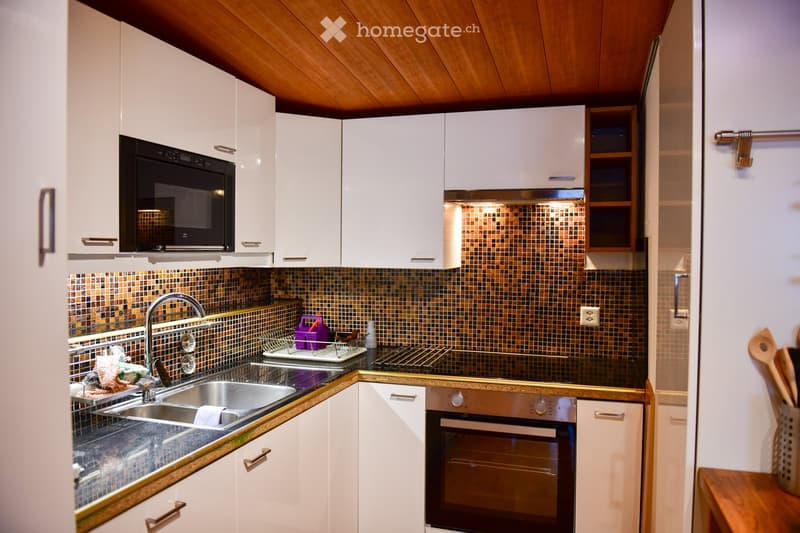white cabinets, tiled backsplash, modern kitchen set up, black countertops, stainless steel sink, black microwave, oven and hob, electrical outlet