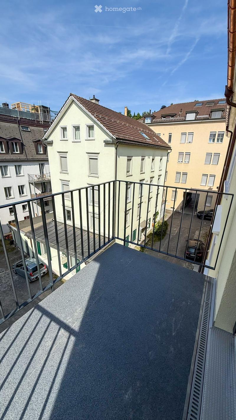 Balcony with metal railing overlooking a residential area with multiple buildings and parked cars.