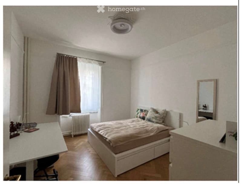 Cozy bedroom with a bed, desk, chair, mirror, radiator, and window with curtains.