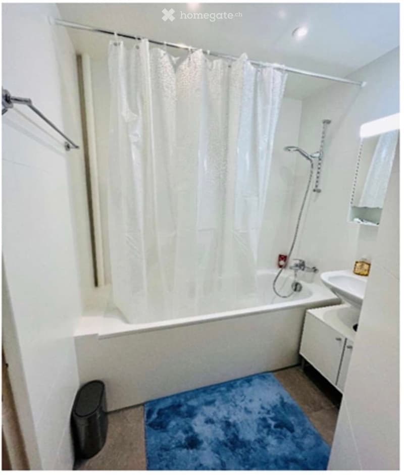 Modern bathroom with a bathtub, shower curtain, sink, cabinet, and a blue rug on the floor.