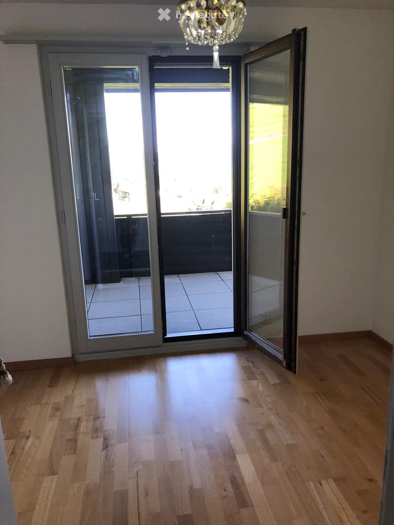Empty room with wooden flooring and large sliding glass doors leading to a tiled balcony area.