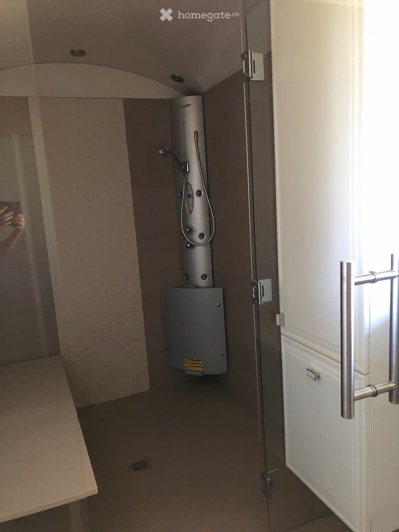 A small bathroom with a modern shower and a water heater unit mounted on the wall. The space features tiled walls and a tiled floor.