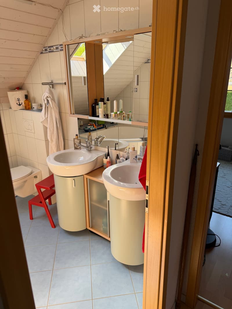 Modern bathroom with double sinks, a large mirror, a toilet, a red stool, and various toiletries on the counter.