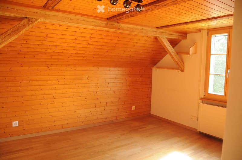 Empty room with wooden walls and ceiling, wooden floor, and a window with a view of greenery.