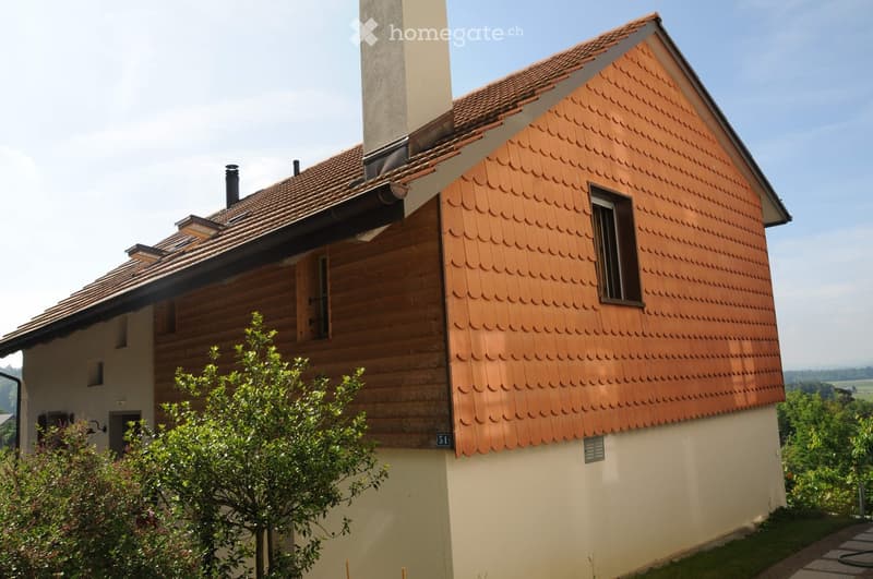 Two-story house with wooden siding and red-tiled roof, featuring multiple chimneys and windows.