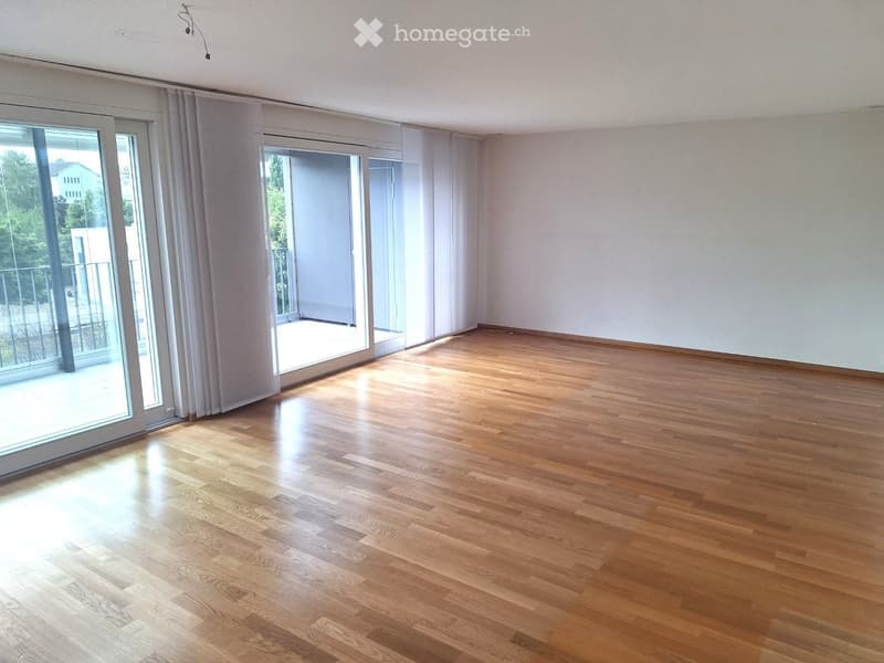 Empty room with wooden flooring, large sliding glass doors leading to a balcony, and white walls.
