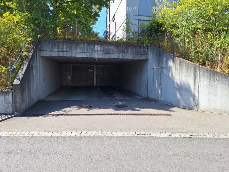 Underground parking entrance with concrete walls and a raised ground floor leading up to a modern building.